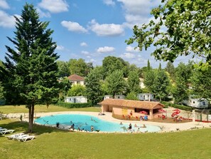 A swimming pool surrounded by grass, trees, and a building with outdoor seating.
