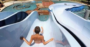 A water slide with a person at the top, surrounded by multiple pools.