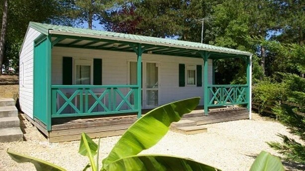 A small, single-story building with a porch and a covered area, surrounded by trees and gravel.