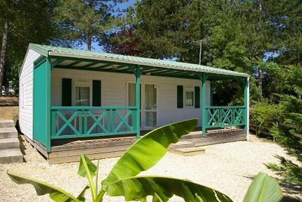 A small, single-story building with a porch and a covered area, surrounded by trees and gravel.