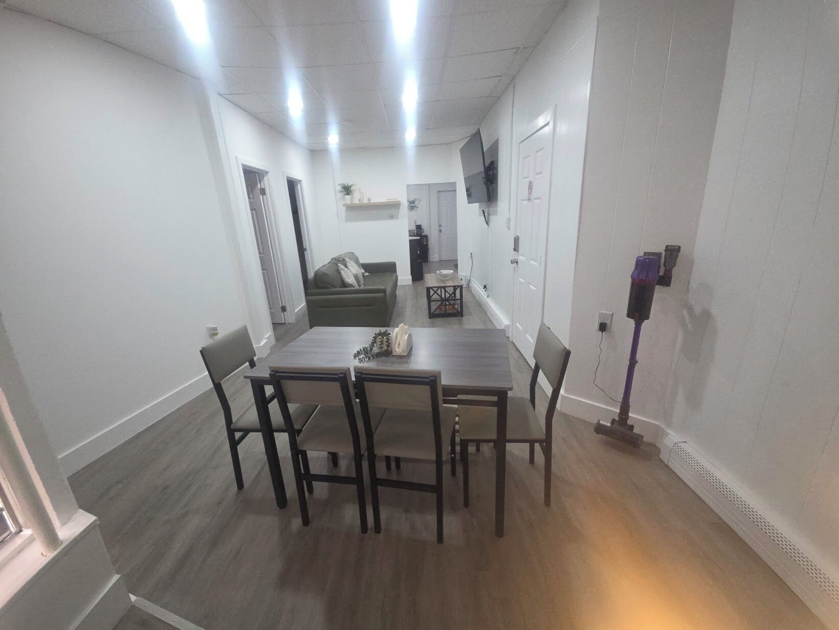 Un comedor con una mesa y sillas de madera, un sofá y un televisor montado en la pared.