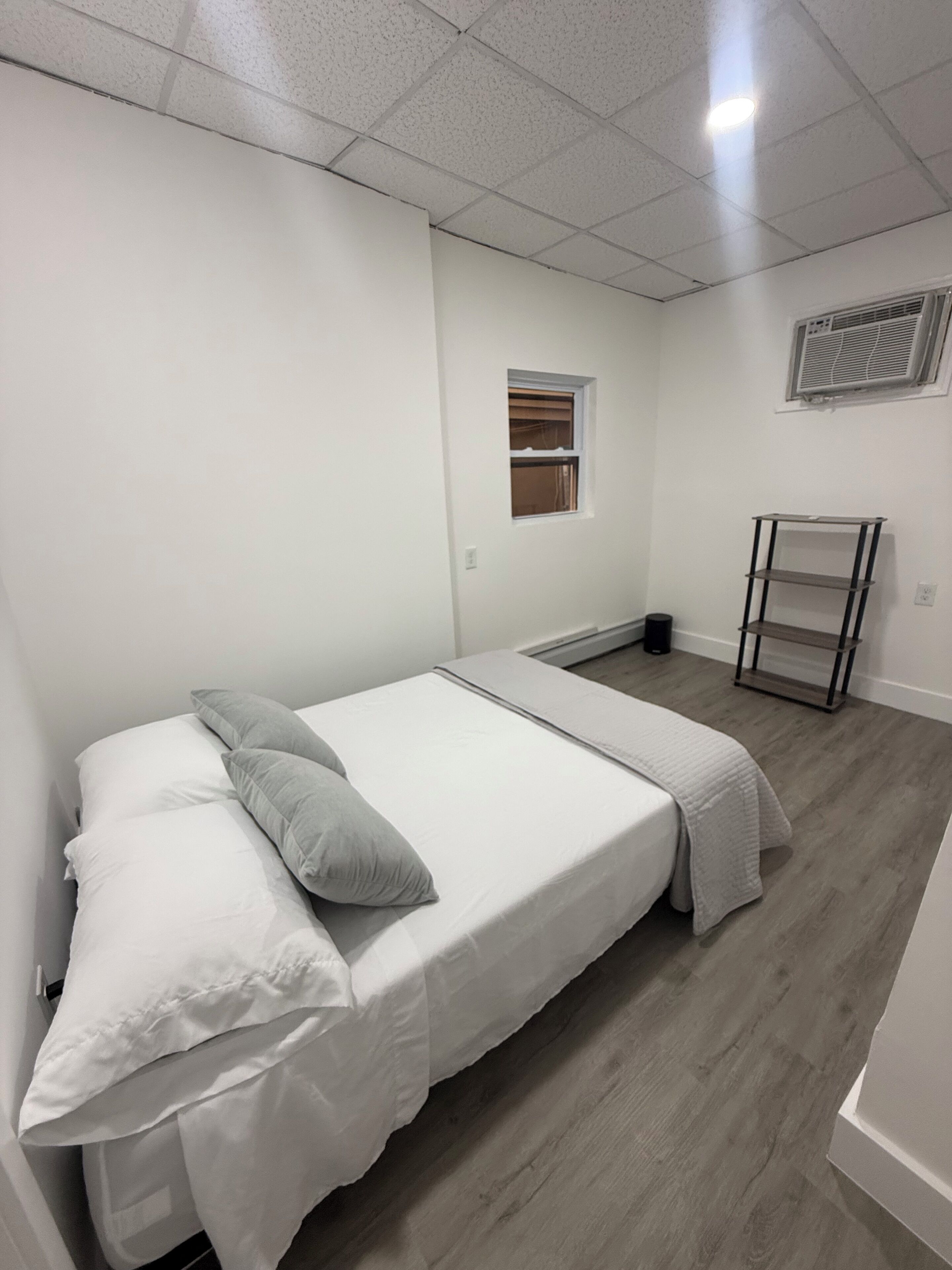 Um quarto com cama, janela, radiador e prateleira.