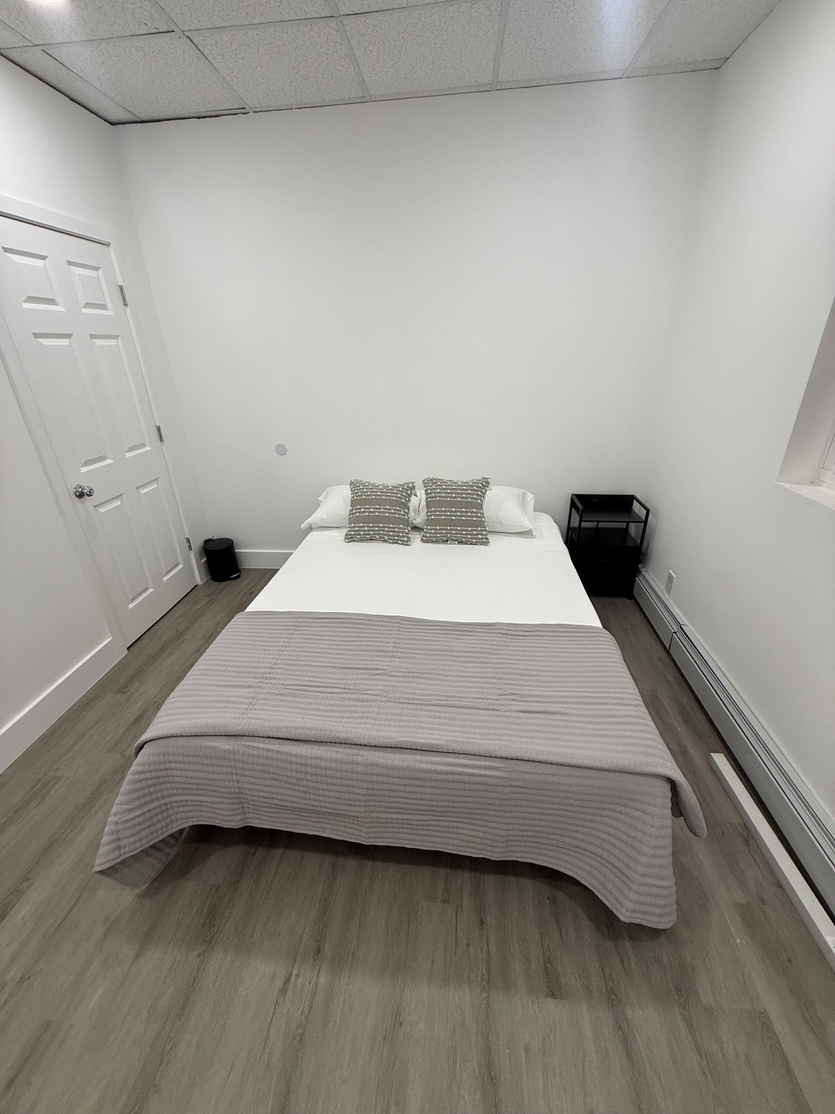 A bedroom with a bed, pillows, a small table, and a heater.