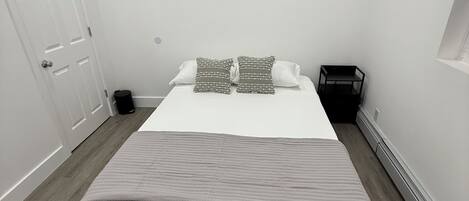 A bedroom with a bed, pillows, a small table, and a heater.