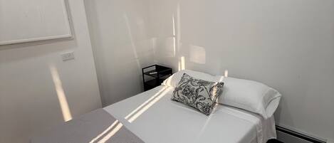 A hotel room with a bed, a bedside table, a nightstand, and a wall-mounted light fixture.
