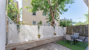 A backyard with a white lattice fence, a concrete patio, and a table with chairs. - Spacious 3-bedroom apartment in gorgeous West New York with AC (West New York)