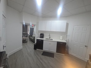 A compact kitchen with white cabinets, a black dishwasher, and a countertop with a coffee maker.