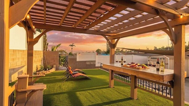 Een terras buiten met een pergola, een eettafel met eten en drinken, en een gazon.