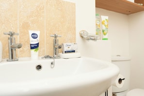 Een badkamer met een wastafel, twee kraan, een zeepdispenser en een toiletrolhouder.