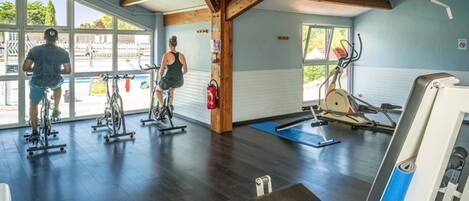 Un gimnasio con bicicletas estáticas, cinta de correr y banco.