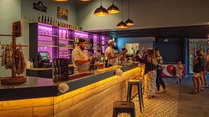 Un'area bar con un bancone in legno, sgabelli da bar e una selezione di bottiglie e bicchieri.