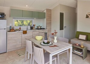 A compact kitchen with a dining area, a small seating area, and a view of greenery outside. - Camping 4 étoiles - Parc aquatique - ccbeifa (Saint-Hilaire-de-Riez)