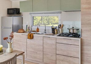 A compact kitchen with a refrigerator, microwave, sink, and stove. - Camping 4 étoiles - Parc aquatique - ccbeifa (Saint-Hilaire-de-Riez)