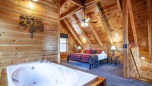 A log cabin interior with a bedroom, a bathroom with a large bathtub, and a wooden ceiling.