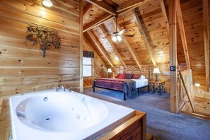 Interior de una cabaña de troncos con un dormitorio, un baño con una bañera grande y techo de madera.