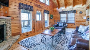 A log cabin interior with a stone fireplace, wooden walls, a stone bench, a leather sofa, and a dining table.