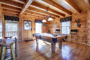 Un interno in legno con tavolo da biliardo, sedie e zona bar.