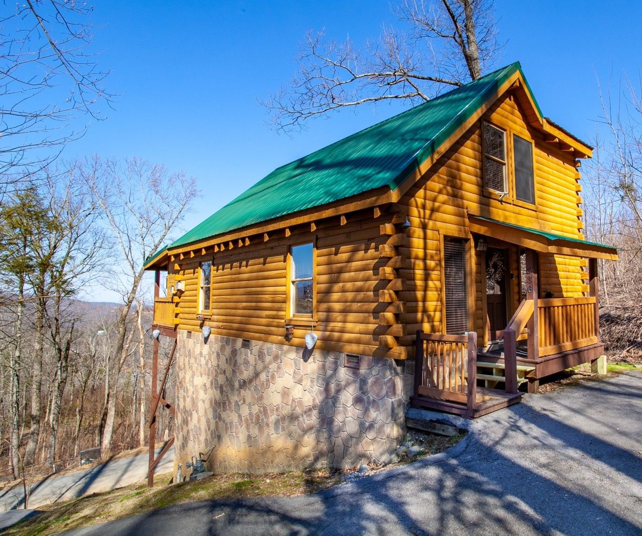 A log cabin with a green roof, a porch, and a stone foundation.