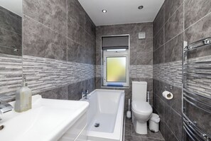 Ein modernes Badezimmer mit Badewanne, Toilette und einem Fenster mit Aussicht.