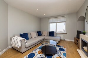Ein modernes Wohnzimmer mit einem Ecksofa, einem Glastisch, einem Kamin und einem großen Fenster.