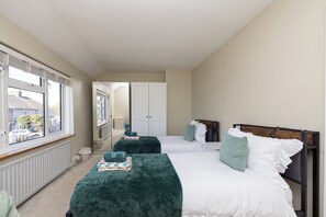 Ein Schlafzimmer mit zwei Betten, einem Heizkörper, einem Fenster und einer Tür zu einem anderen Raum.