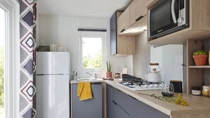Moderni keittiö, jossa on jääkaappi, liesi, mikroaaltouuni ja ikkuna, josta avautuu näkymä vehreään maisemaan.