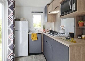 Eine moderne Küche mit Kühlschrank, Herd, Mikrowelle und einem Fenster mit Blick ins Grüne.