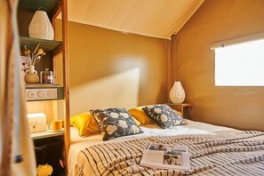 Ein gemütliches Schlafzimmer mit Bett, Kissen, einem Nachttisch mit Lampe und einem Fenster.
