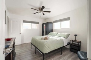 Ein Schlafzimmer mit Bett, Deckenventilator, Kleiderschrank, Nachttisch und Schreibtisch.