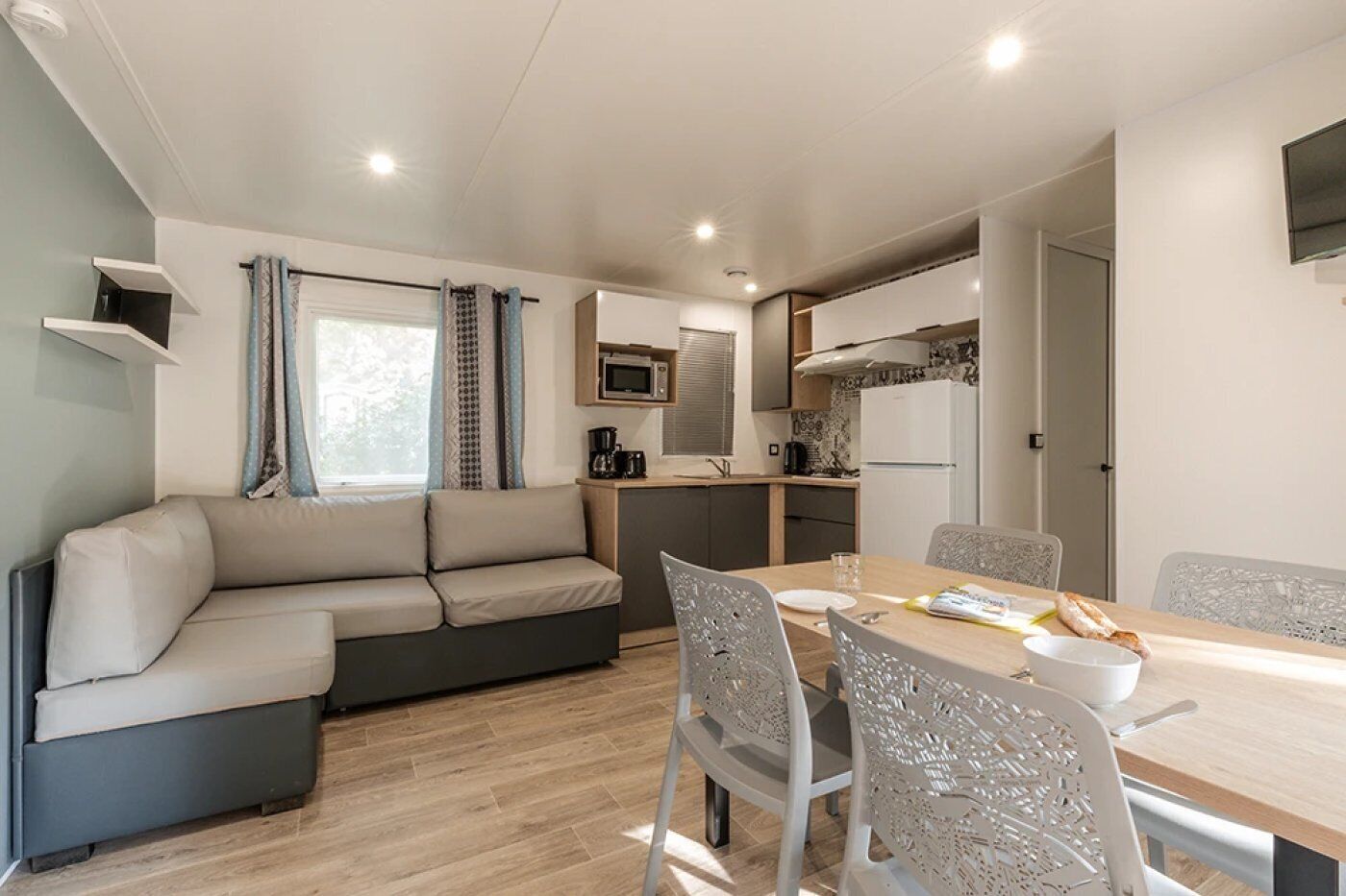 A compact living space with a sofa, dining table, chairs, a kitchenette, and a TV mounted on the wall.