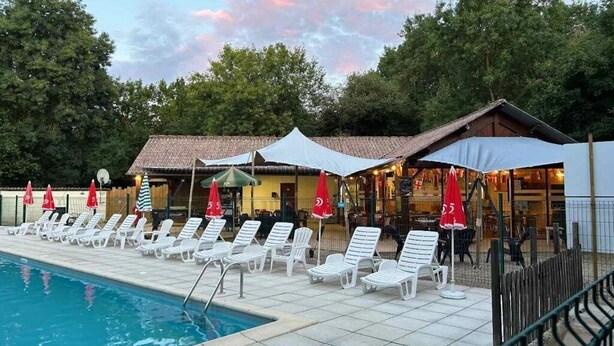 A pool area with lounge chairs and umbrellas, a building with a tiled roof, and trees in the background. - Camping 4 étoiles - Piscine  - ccbgagb (Concourson-sur-Layon)