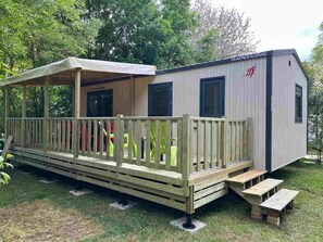 Ein Mobilheim mit überdachter Veranda, einer kleinen Terrasse und einer Rampe zum Eingang.
