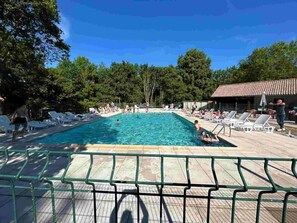 Ein rechteckiger Swimmingpool, umgeben von Liegestühlen und einem überdachten Bereich mit Ziegeldach.