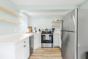 Eine kompakte Küche mit weißen Schränken, einem Edelstahl-Kühlschrank, einem schwarzen Backofen und einer Holz Arbeitsplatte.