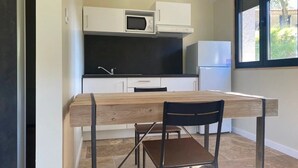 Kompakti keittiö, jossa on valkoiset kaapit, mikroaaltouuni, jääkaappi ja ruokapöytä tuoleineen.