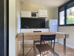 Una cocina compacta con armarios blancos, un microondas, un refrigerador y una mesa de comedor con sillas.