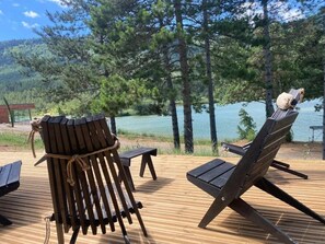 Una terraza de madera con dos sillas Adirondack mirando a un lago, rodeado de árboles.