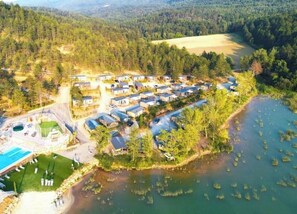 An aerial view of a lakeside resort with multiple cabins, a swimming pool, and a forested backdrop. - Villa 4 étoiles - Piscine  - ccbgccd (Arques)