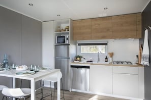 A modern kitchen with white cabinetry, a stainless steel refrigerator, a dishwasher, and a window above the sink. - Camping 4 étoiles - Piscine  - ccbgccg (Arques)