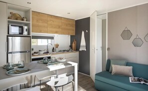 A compact kitchen with modern appliances, a dining area with a white table and chairs, and a teal sofa with a magazine. - Camping 4 étoiles - Piscine  - ccbgccg (Arques)