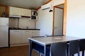 Ett kompakt kök med mikrovågsugn, spis och skåp. Det finns ett matbord med stolar.