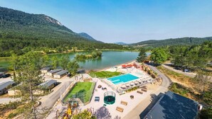Un resort con piscina, cancha de tenis y vistas a un lago rodeado de montañas.