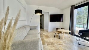 A modern living room with a sofa, a dining table, a TV, and a large window.