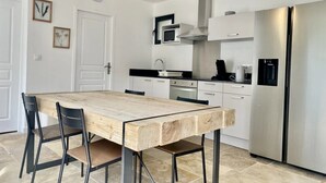 A modern kitchen with a wooden dining table, chairs, a stainless steel refrigerator, and a ceiling light fixture.