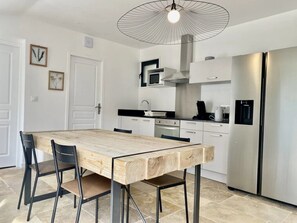 Een moderne keuken met een houten eettafel, stoelen, een roestvrijstalen koelkast en een plafondlamp.