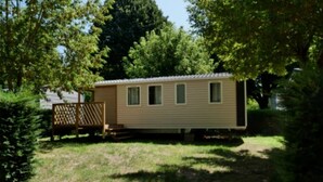 Une maison mobile avec une cour clôturée, entourée d’arbres et sous un ciel dégagé.