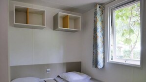 Une chambre avec deux lits, une fenêtre donnant sur la verdure et des étagères intégrées au-dessus des lits.