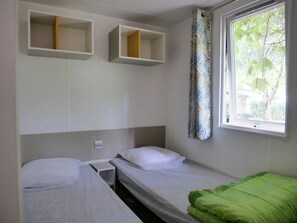 Ein Zimmer mit zwei Betten, einem Fenster mit Blick auf Bäume und eingebauten Regalen über den Betten.