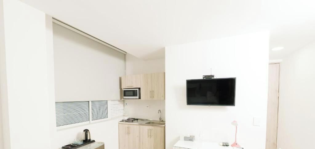 Una cocina compacta con microondas, estufa y lavabo, un televisor de pantalla plana montado en la pared, y una puerta que da a otra habitación.