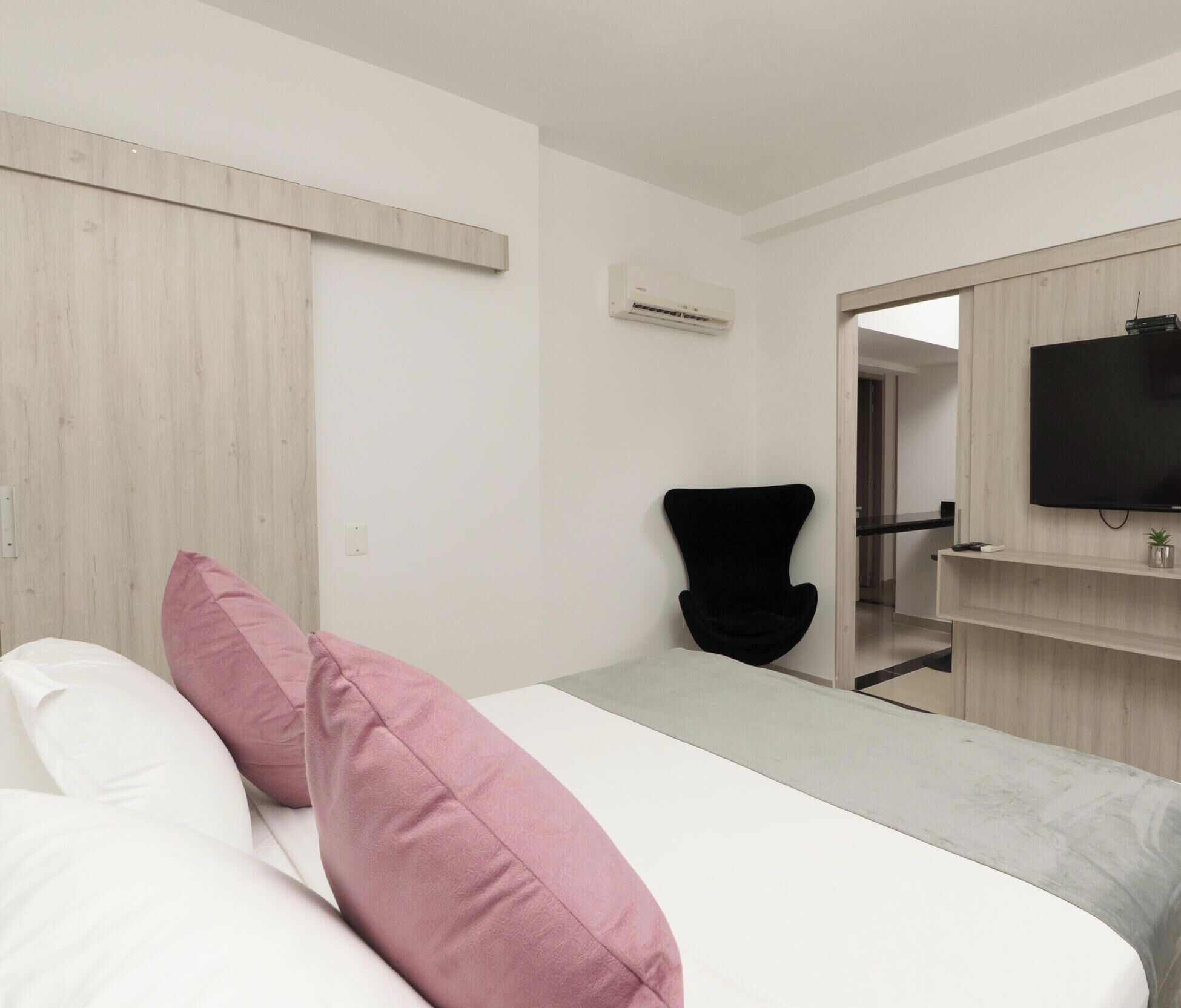 Habitación de hotel con cama, una silla, televisor y un panel de pared de madera.